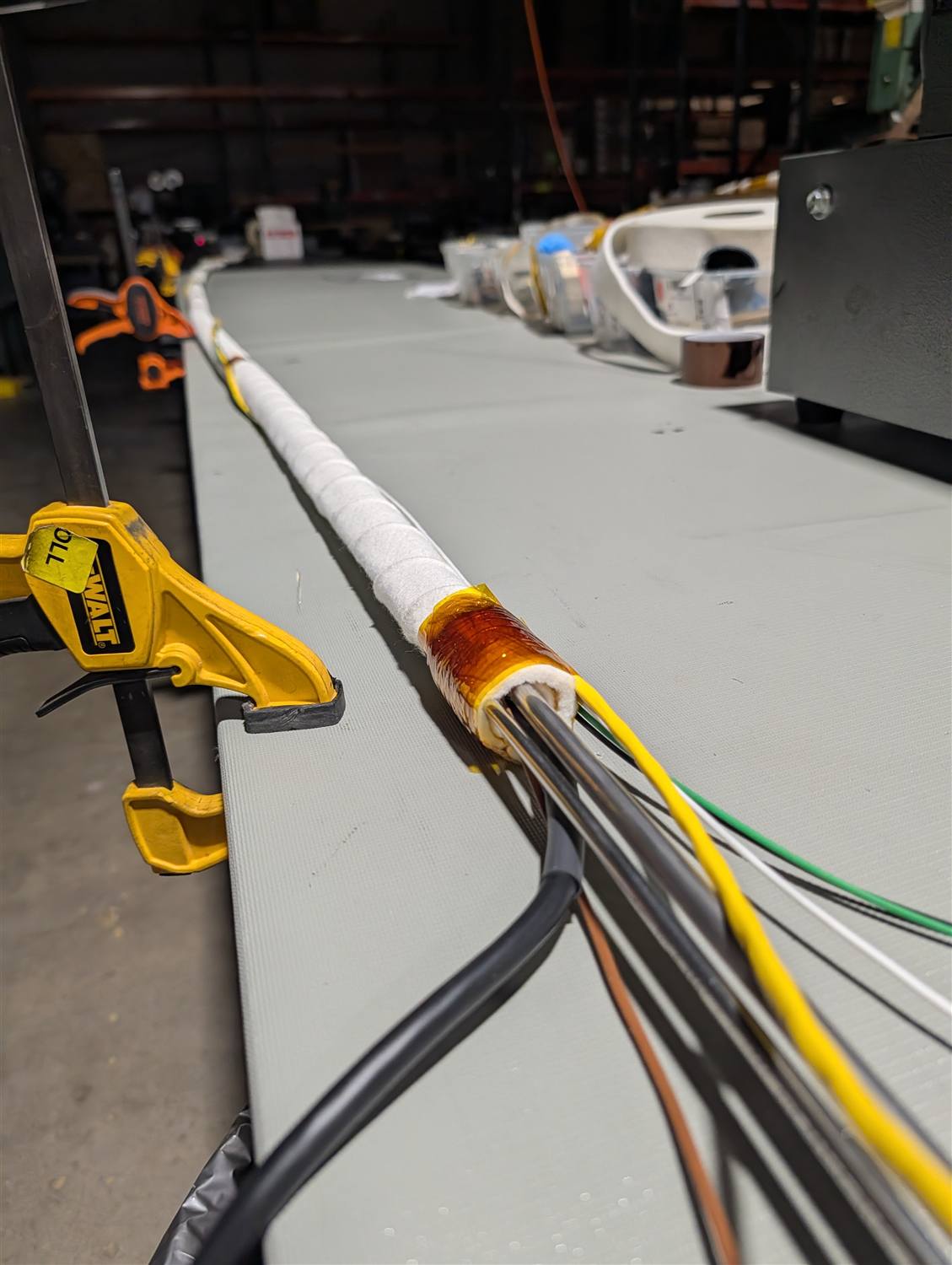 A process tube clamped mid-wrap with felt insulation applied and several colored signal wires fanning out